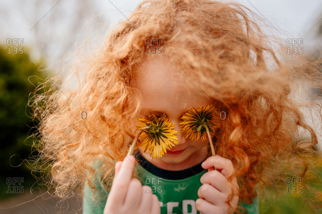 Child with dandelions covering eyes