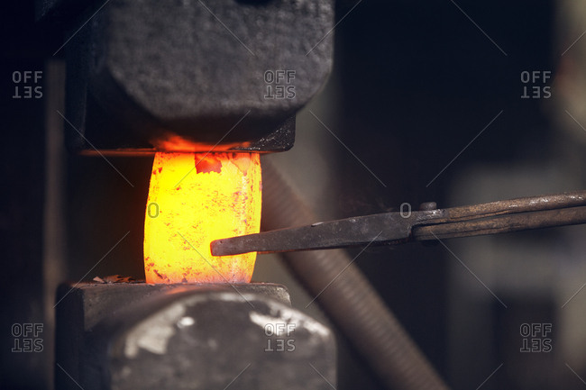 Close-up of hot red metal held by tongs in metal industry