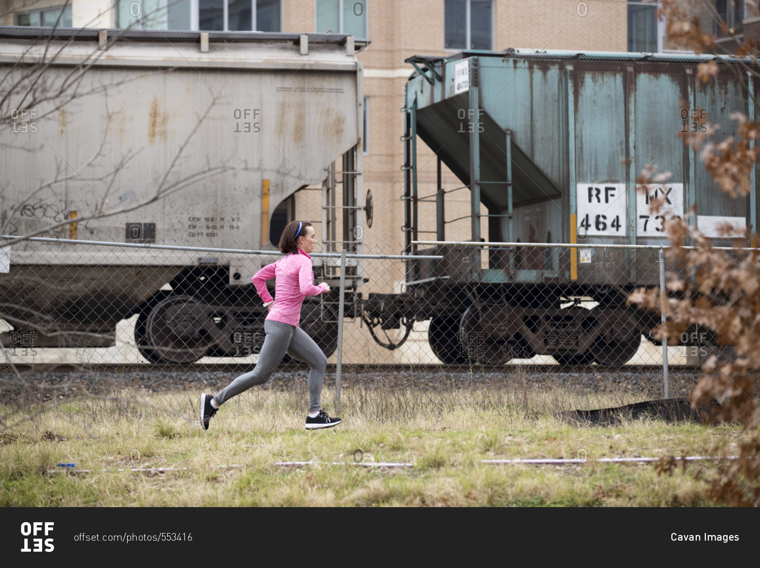 Side view of woman jogging on grassy field by freight train