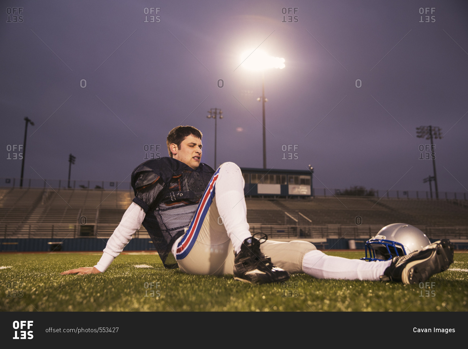 American football player relaxing on grassy field at stadium against sky