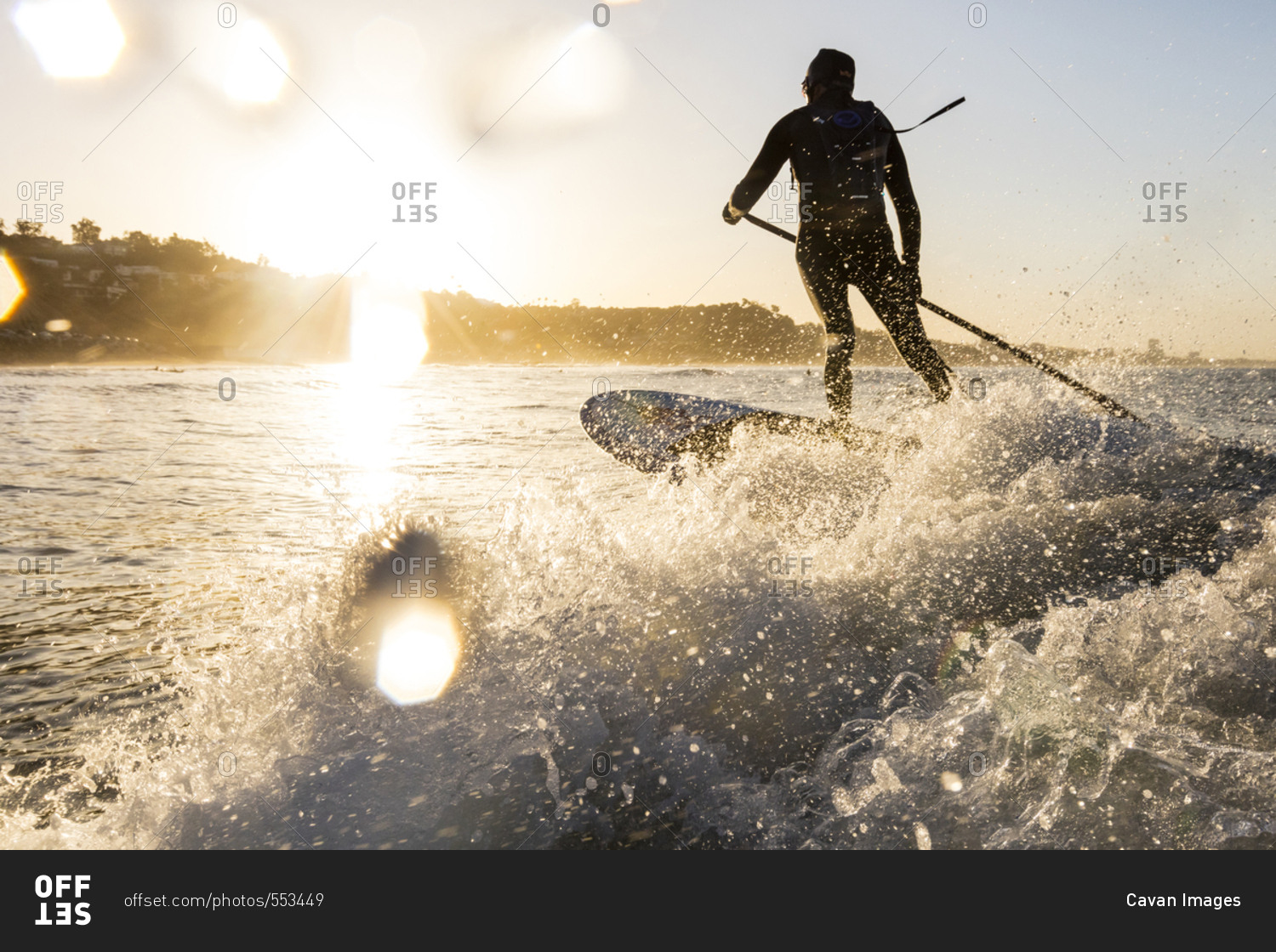Rear view of man holding pole while surfing in sea during sunset