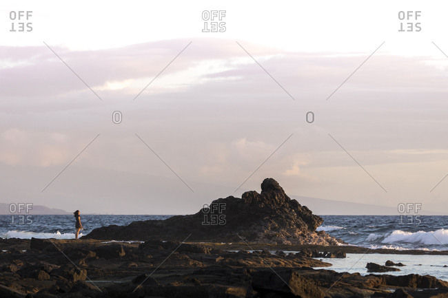 Distant view of woman standing on rock by sea against cloudy sky