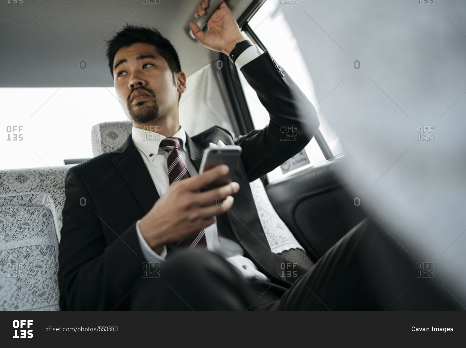 Thoughtful businessman holding smart phone while sitting in taxi