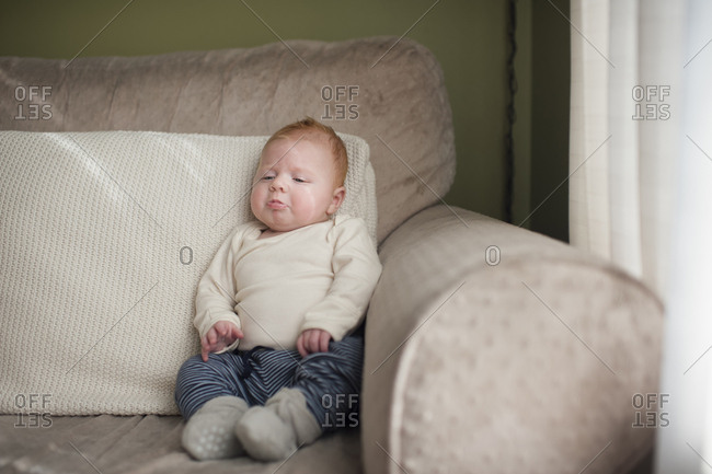 Cute baby boy frowning while sitting on sofa at home