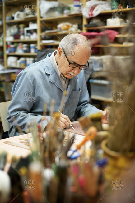 Senior artist carving bas relief while working at table in workshop