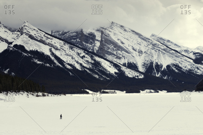 Distant view of woman walking on snow covered landscape against cloudy sky