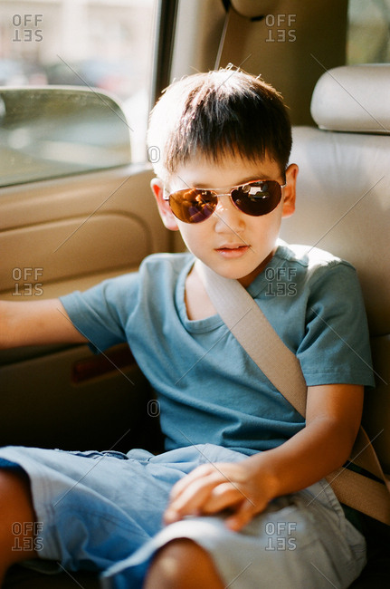 Young boy in sunglasses wearing seat belt in back seat