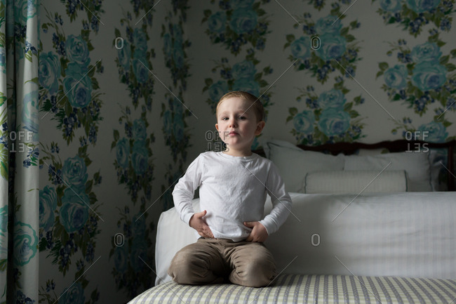 Boy on bed in room with flowered wallpaper