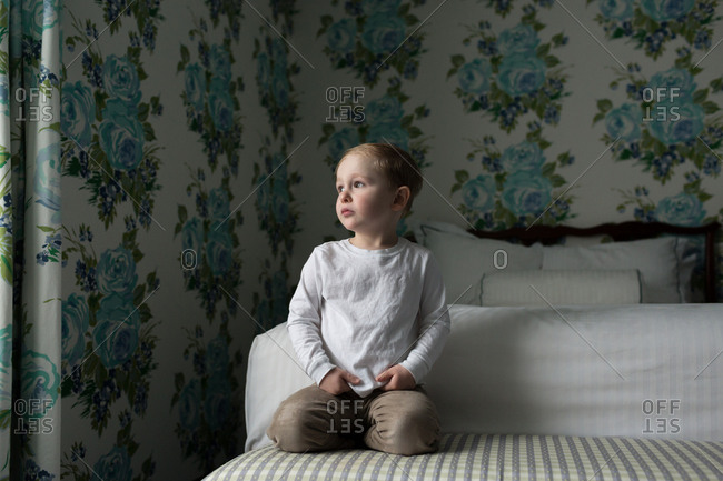 Boy on bed in room with blue flowered wallpaper