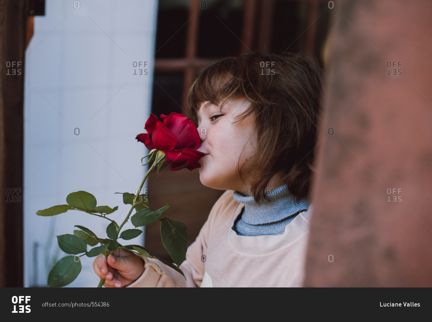 Young girl stiffing a red rose in garden