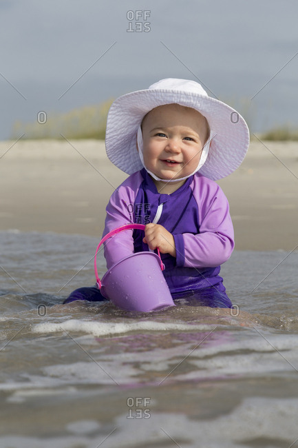 A young girl plays on a beach with plastic pail