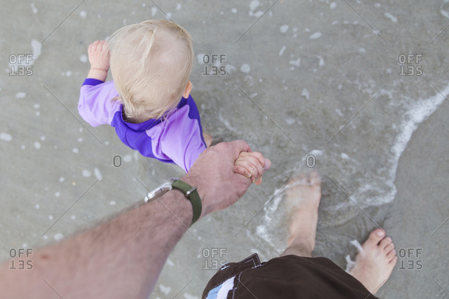 Overhead view of father holding baby girl's hand while walking on beach