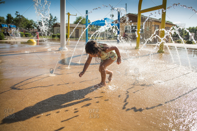 Girl running through water fountains on splash pad