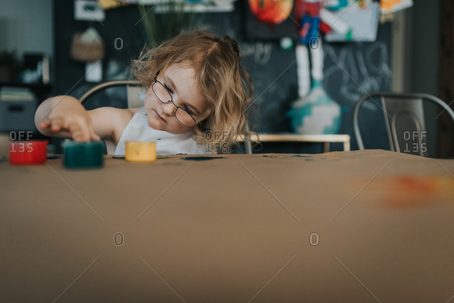 Little girl with glasses playing with finger paints at table