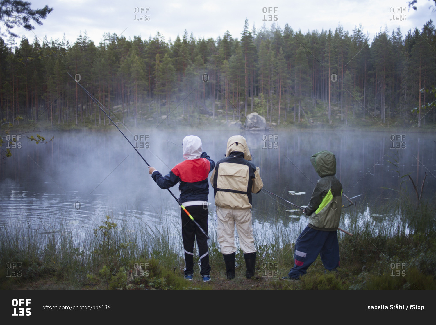 Rear view of children wearing raincoats fishing at lake in foggy weather