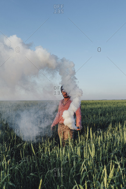 Man standing with distress flare emitting smoke on field against blue sky