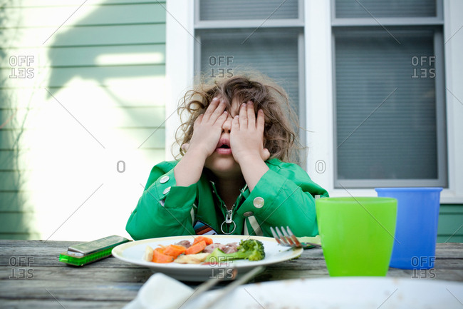 Young girl covering face with hands at picnic table