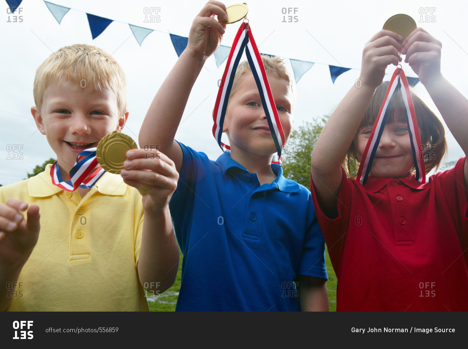 Three children holding sports medals on the school playing field