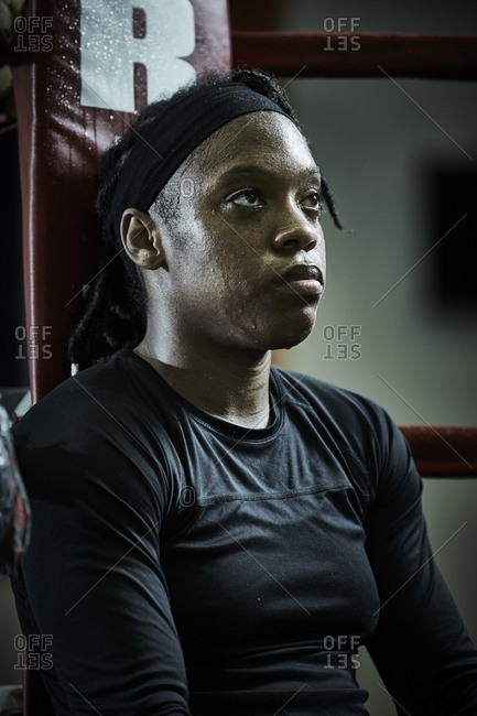 Thoughtful female boxer looking away while sitting in boxing ring at health club