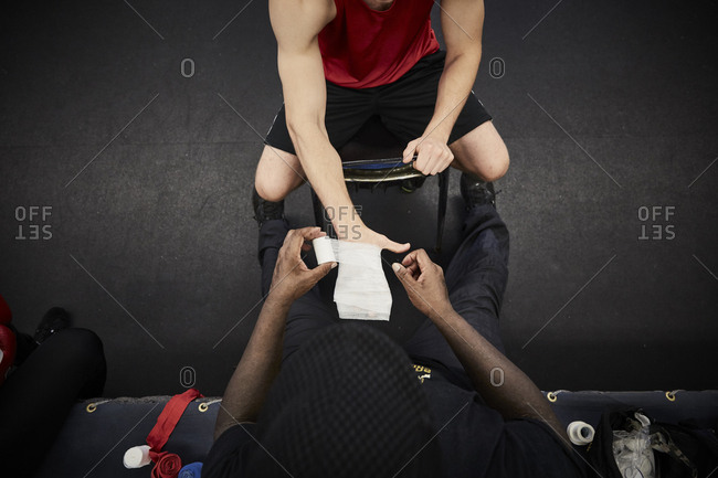 High angle view of coach wrapping bandage on male boxer\'s hand at health club