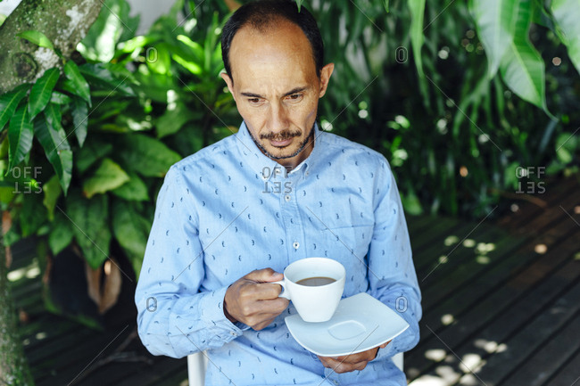 Portrait of a pensive mid aged man having a cup of coffee on a terrace of Medellin, Colombia