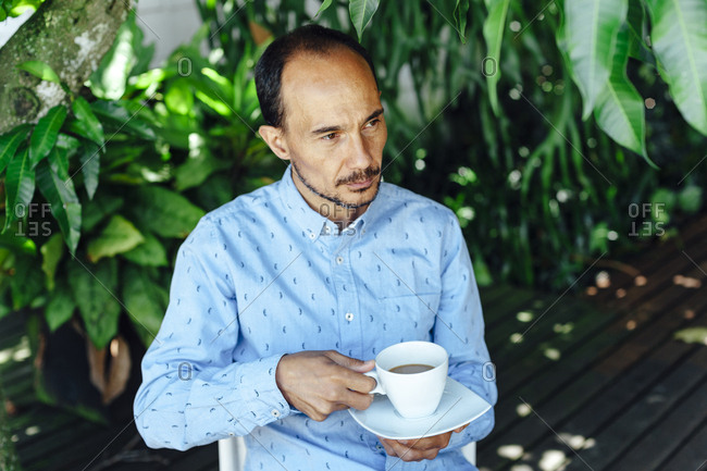 Portrait of a pensive mid aged man having a cup of coffee on a terrace of Medellin, Colombia