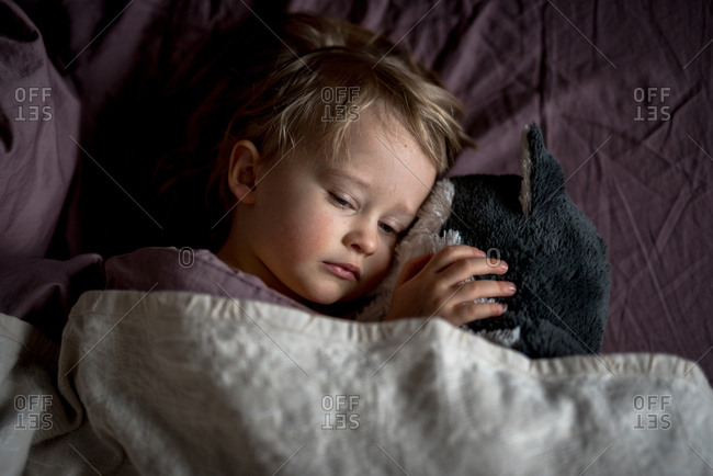 Sleepy child cuddling with stuffed animal in bed