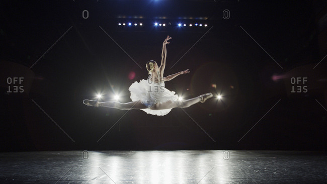 Rear view of serious ballet dancer leaping in costume performing onstage in show