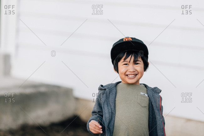 Boy in baseball cap grinning by house