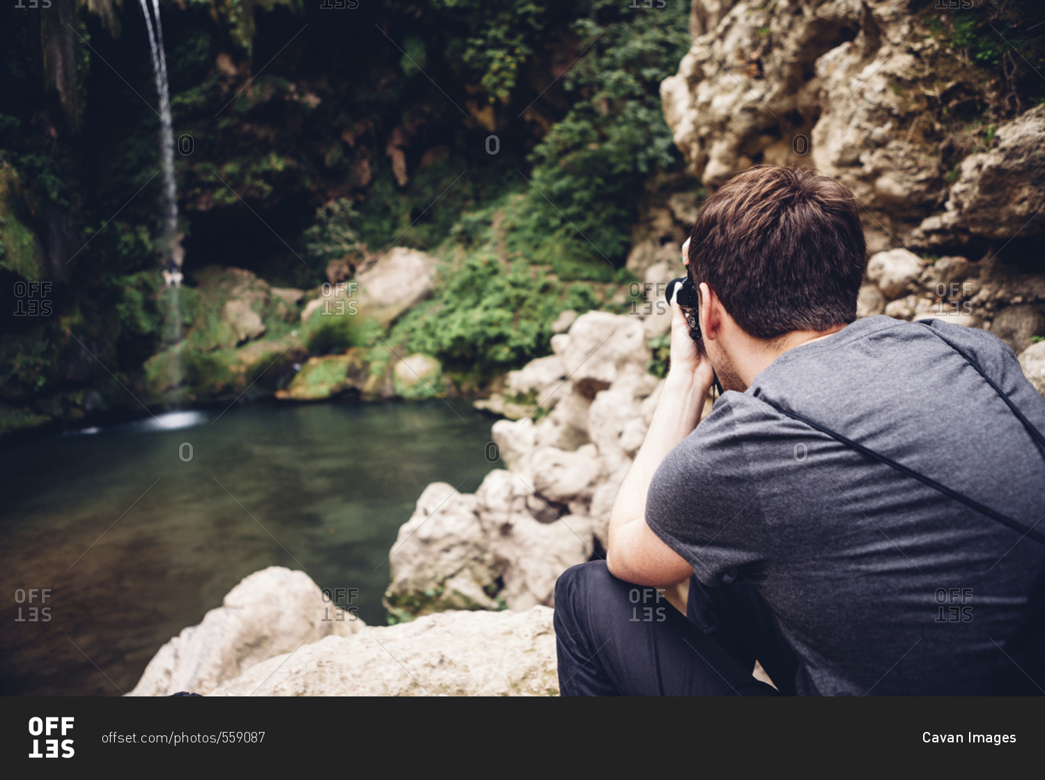 Rear view of male hiker photographing waterfall through camera