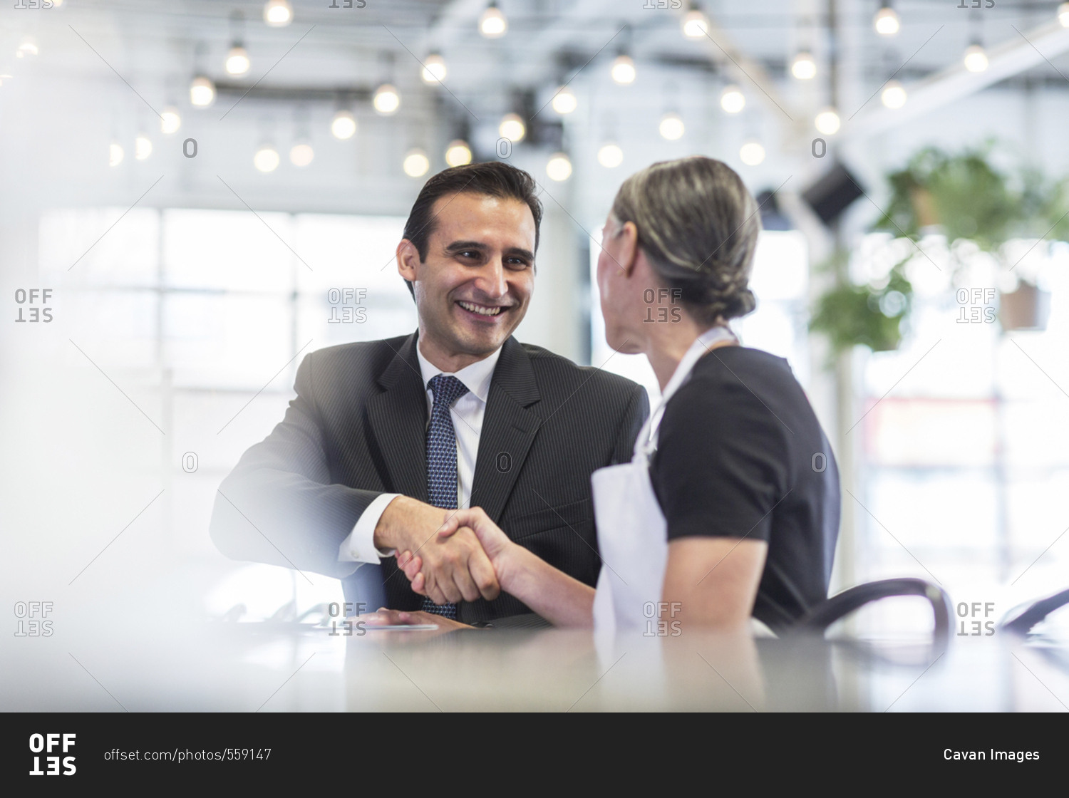 Businessman giving handshake to female chef at table in restaurant