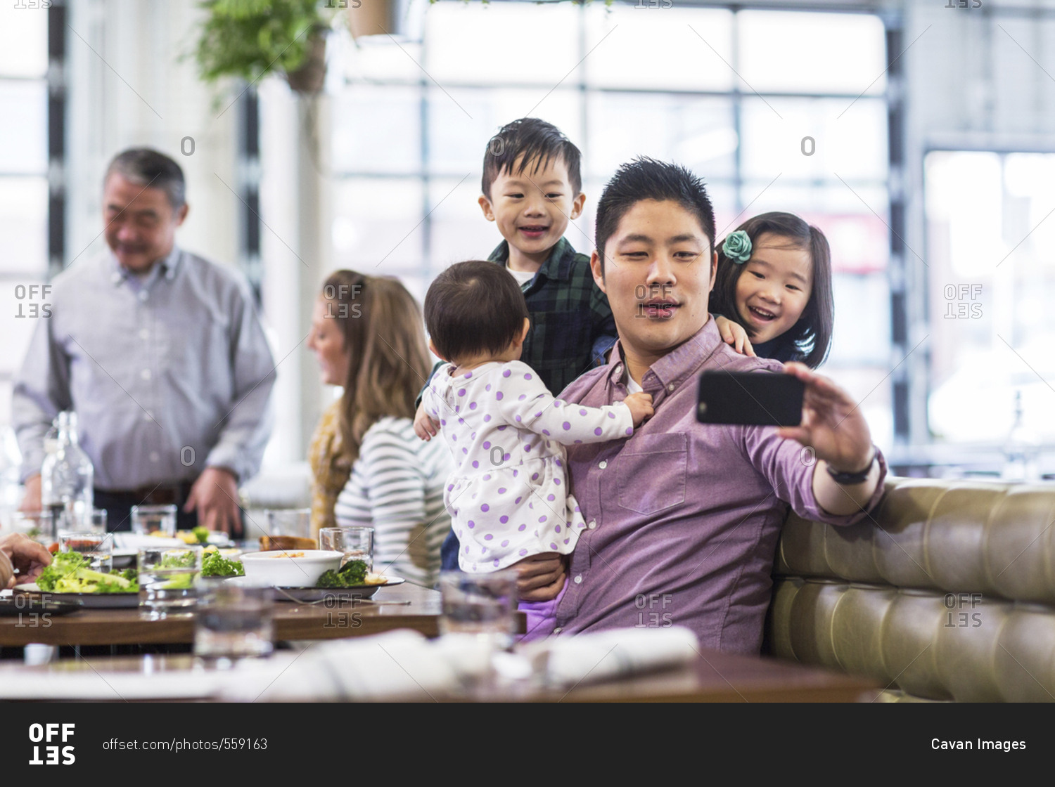 Father taking selfie with children while sitting with family in restaurant