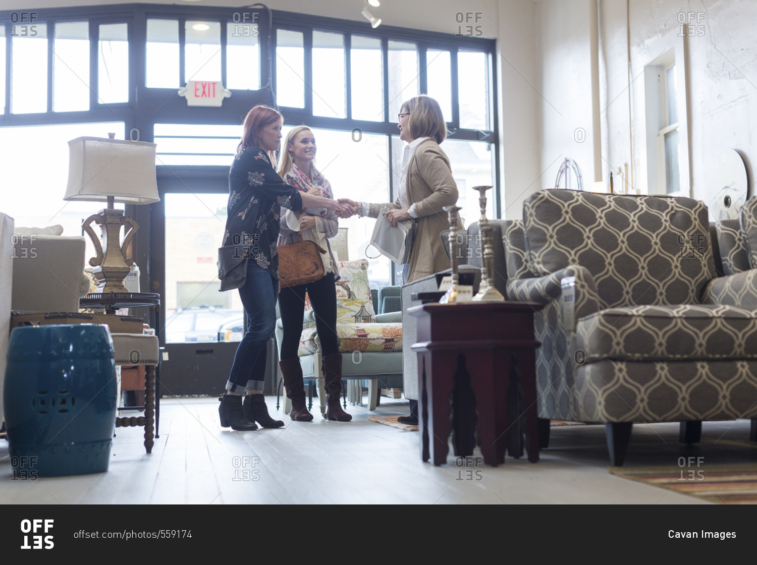 Woman looking at owner doing handshake with friend in furniture store