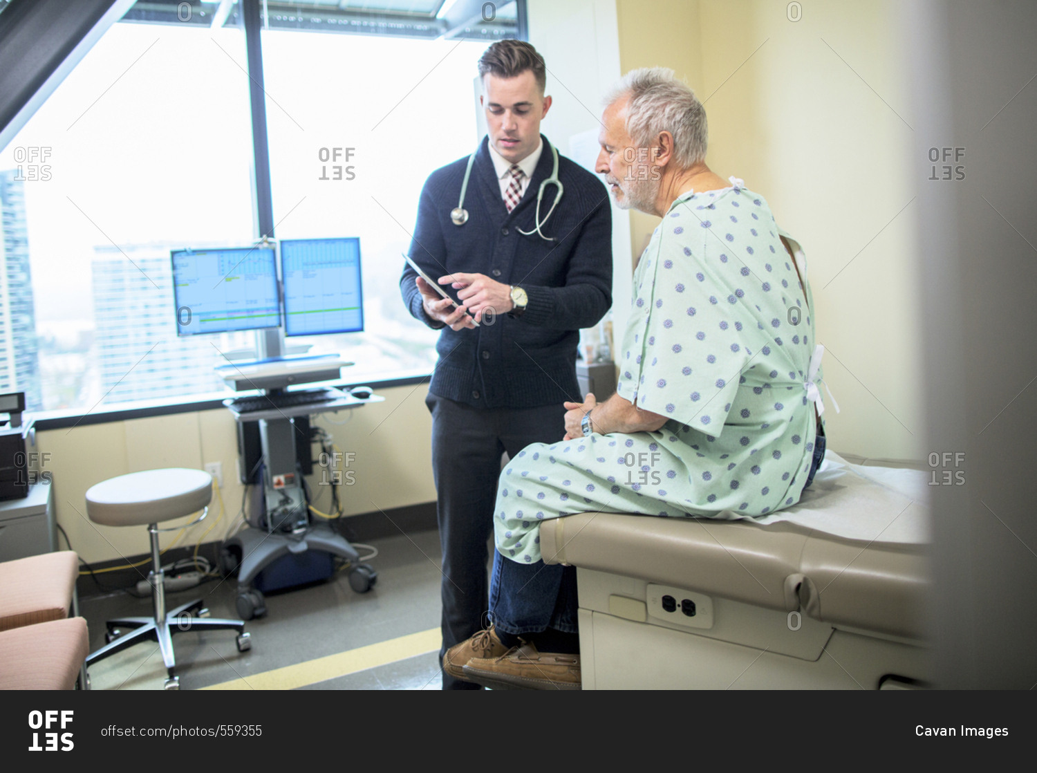 Male doctor explaining to patient over tablet computer in hospital ward