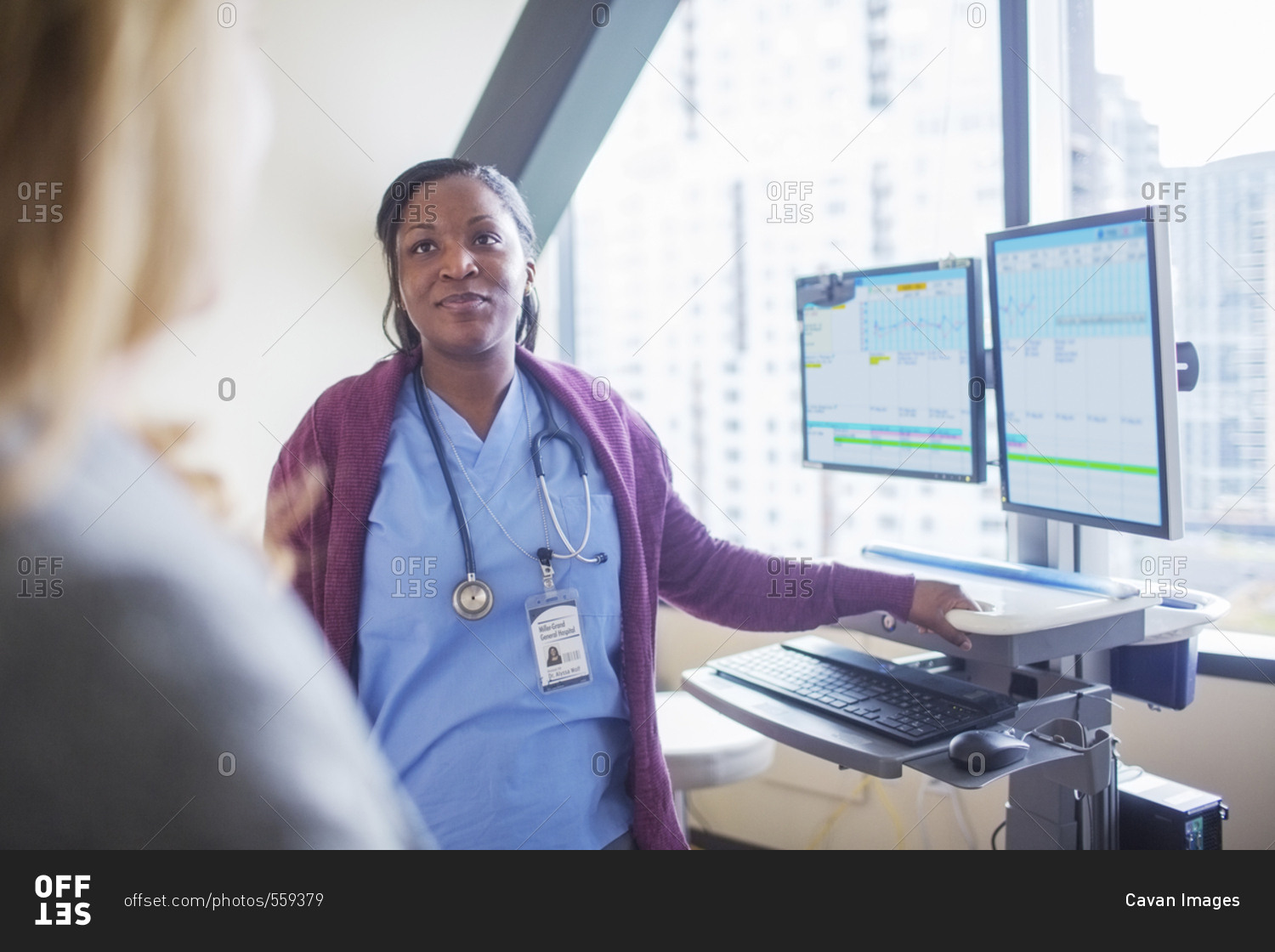 Female doctor looking at patient while standing by desktop computers in medical room