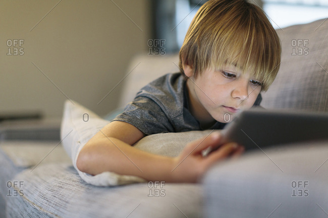 Close-up of boy using tablet computer while lying on sofa at home