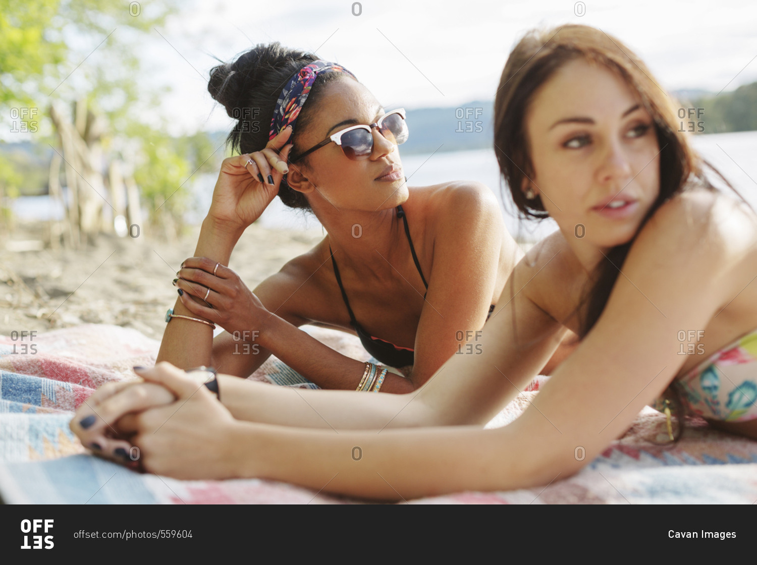 Rear view of female friends sitting on picnic blanket at riverbank