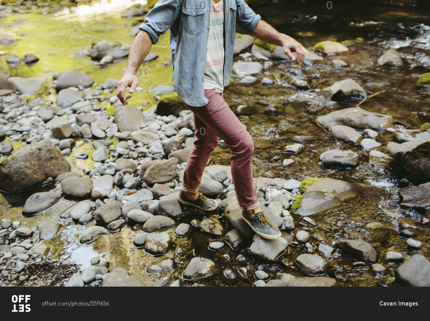 Low section of man walking on rocks in river at forest