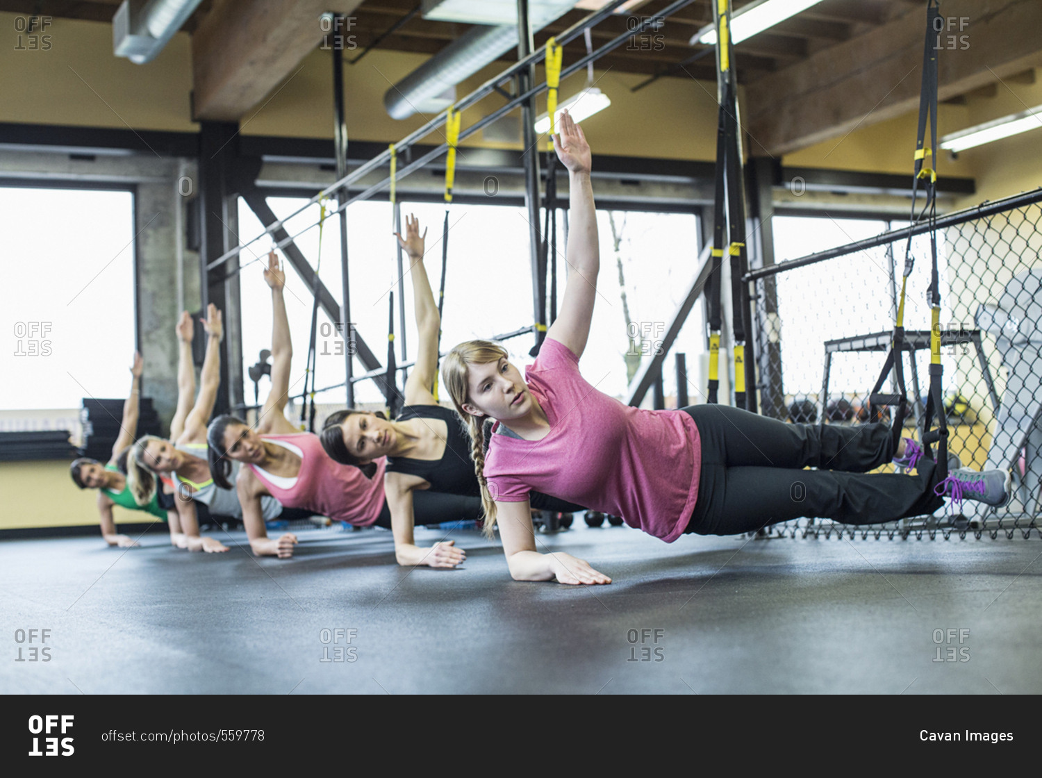 Women practicing side plank pose while balancing on resistance bands in gym