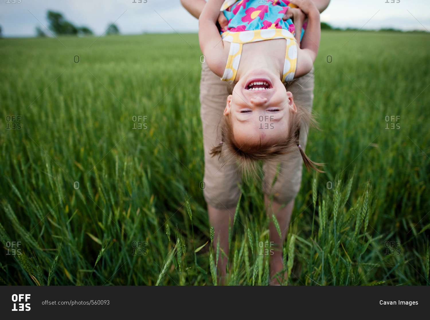 Low section of mother carrying daughter upside down while standing on grassy field