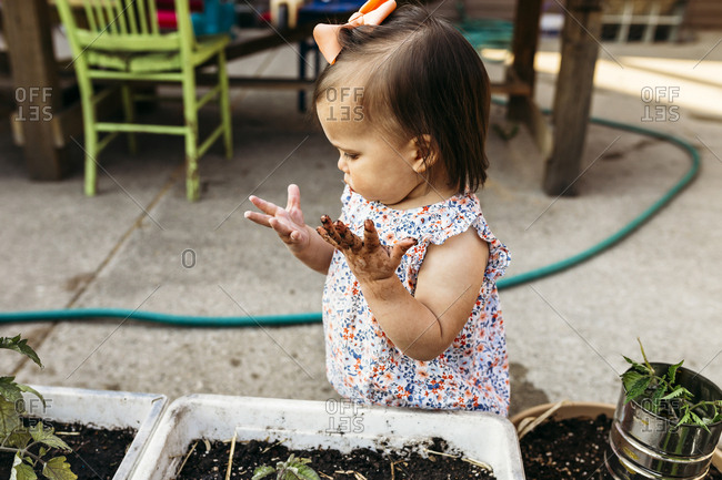 High angle view of baby girl with messy hands standing by potted plants at backyard