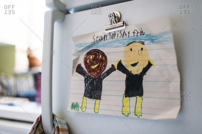Child's drawing of African American and Caucasian friends hung on a refrigerator with a magnet