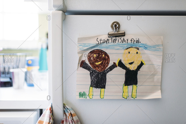 Child's drawing of African American and Caucasian friends hung on a refrigerator with a magnet