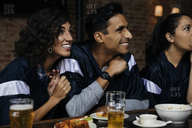Happy man and woman watching sports on TV at bar