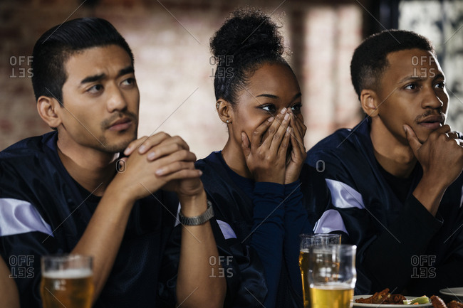 Young woman covering face while watching sports with male friends in bar