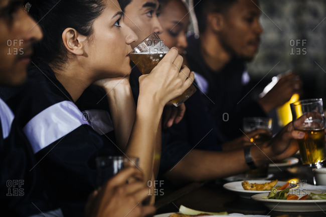 Woman drinking beer while watching sports on TV with friends in bar