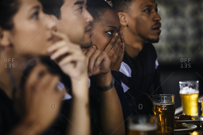 Serious young woman covering face while watching soccer match with friends in bar