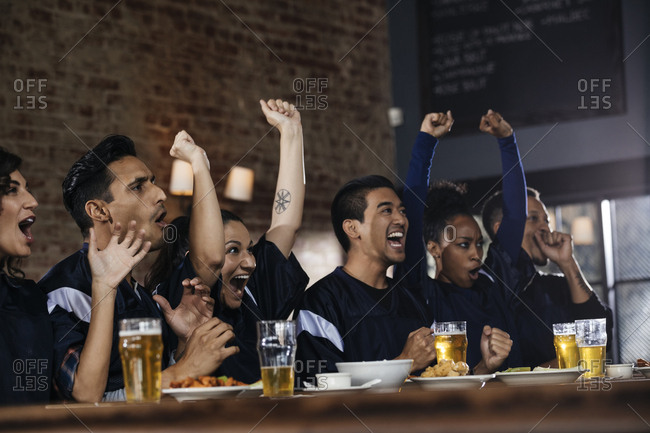 Multiethnic male and female friends screaming while watching soccer match in bar