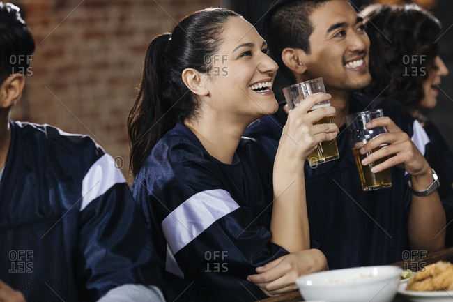 Happy  woman holding beer glass while watching sports on TV with friend in bar