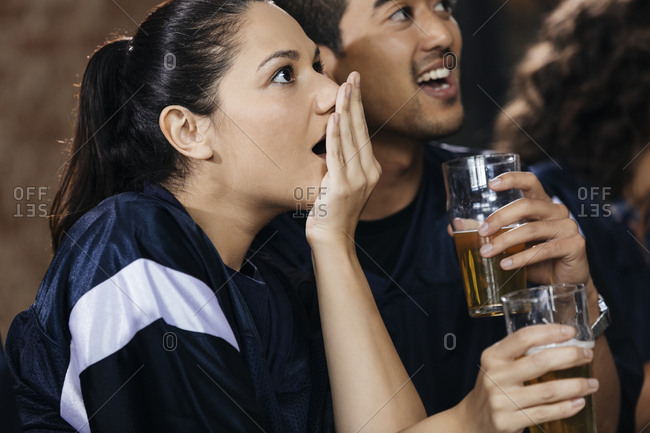 Woman covering mouth while watching soccer match with friend in bar
